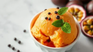 Sorvete De Maracujá Cremoso Fácil Com 4 Ingredientes 48 Tigela branca com sorvete de maracujá alaranjado e aveludado, decorado com sementes frescas e uma folha de hortelã.